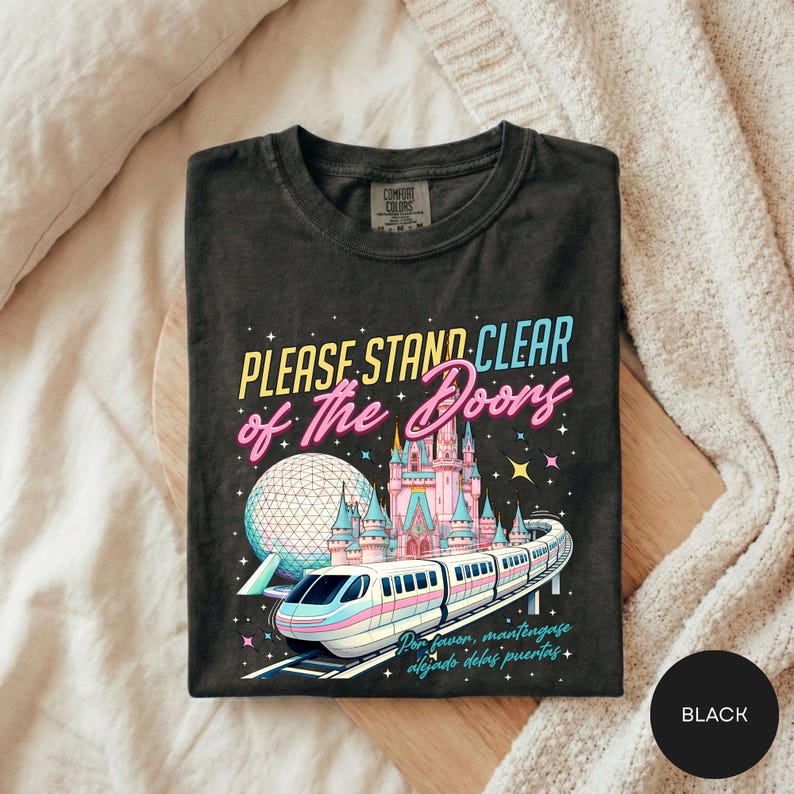A black t-shirt with a colorful graphic design depicting a train and a castle, along with the text "Please Stand Clear of the Doors" and "Disneyland" written on it.