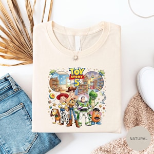 a white t-shirt with a colorful graphic of characters from the Toy Story movie, including Woody, Buzz Lightyear, and other beloved characters.