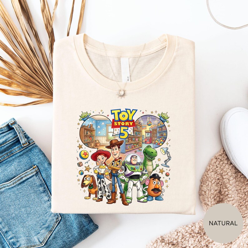 a white t-shirt with a colorful graphic of characters from the Toy Story movie, including Woody, Buzz Lightyear, and other beloved characters.
