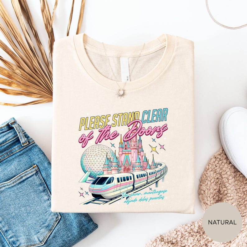a white t-shirt with a colorful graphic design depicting a train and a castle, along with the text "Please stand clear of the doors".