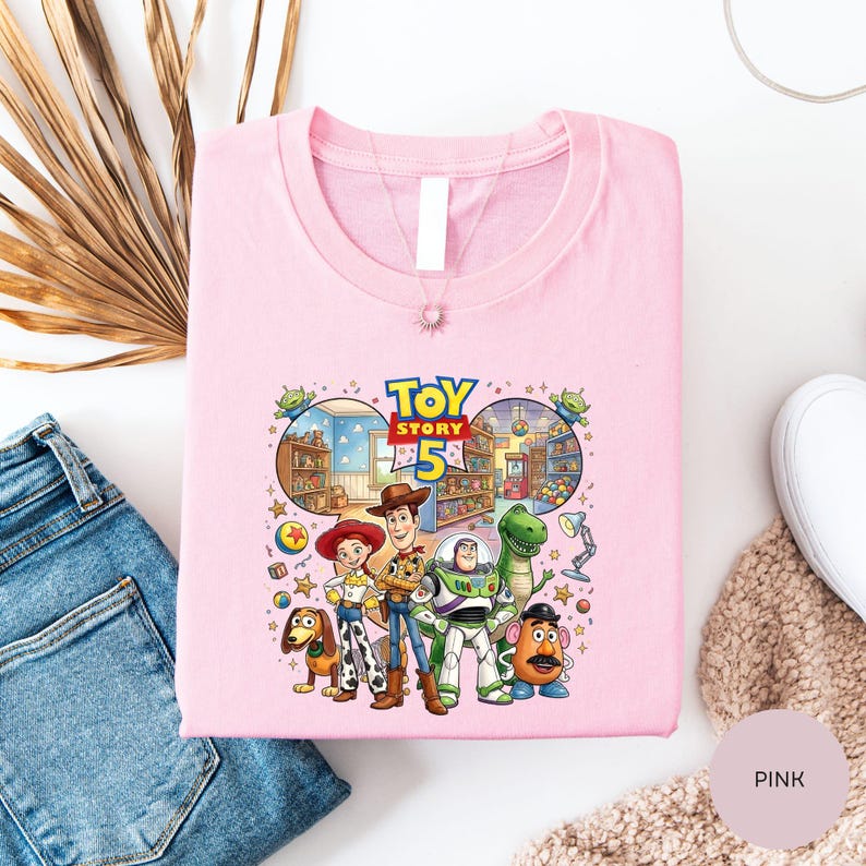 a pink t-shirt with a cartoon illustration of characters from the Toy Story movie, including Woody, Buzz Lightyear, and other beloved characters.
