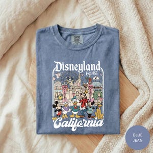 A blue t-shirt with a graphic design of Disney characters and the text "Disneyland Est. 1955 California" printed on it.