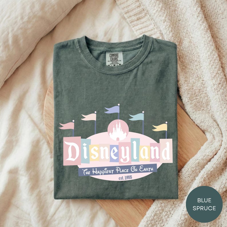 A green t-shirt with a Disneyland logo and text, laid out on a wooden surface.