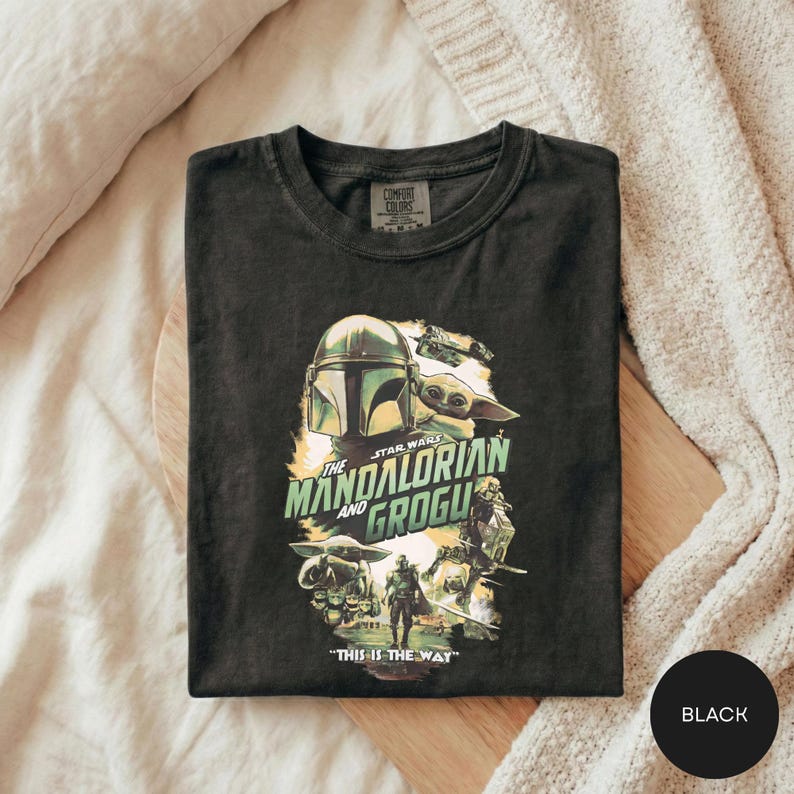 A black t-shirt with a graphic design featuring characters from the Star Wars series, specifically The Mandalorian and the Frogs.
