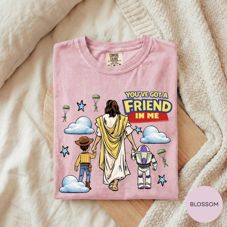 A pink t-shirt with a cartoon illustration of a person holding hands with a child and a robot, along with the text "You've got a FRIEND in ME" and various other cartoon characters.