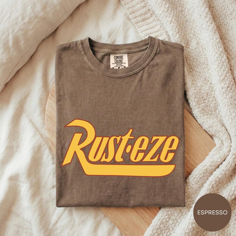 A brown t-shirt with the word "Rusteze" printed on it, laid out on a wooden surface.