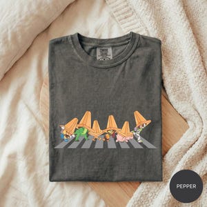 A gray t-shirt with a graphic design depicting a group of cartoon characters crossing a road.