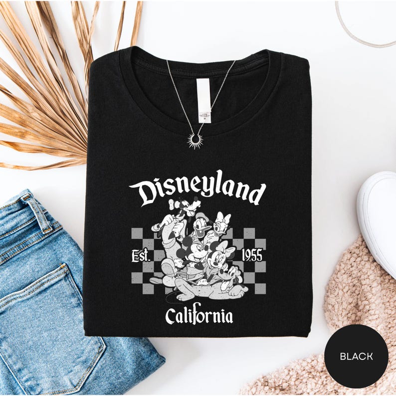 a black t-shirt with a graphic design of Disney characters and text, along with a pair of jeans and some decorative items.