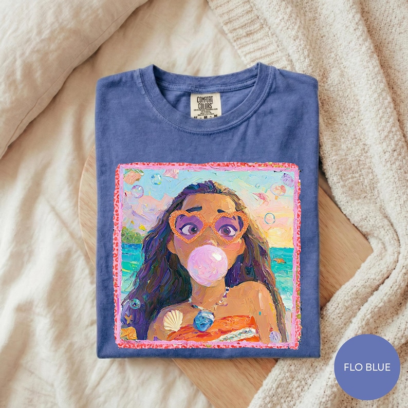 A blue t-shirt with a colorful illustration of a young girl blowing a bubble gum bubble, wearing sunglasses and a necklace.