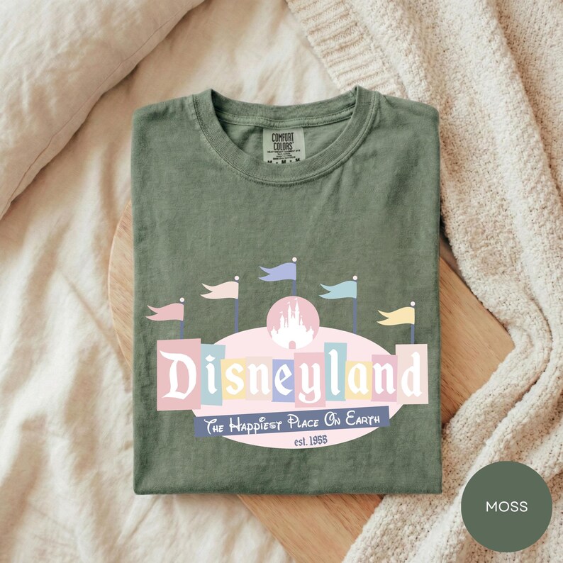 A green t-shirt with a Disneyland logo and text, laid out on a wooden surface.