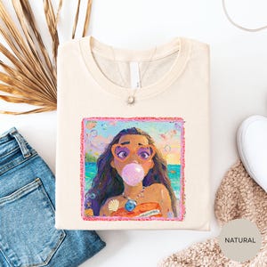 a white t-shirt with a colorful illustration of a woman blowing a bubble gum bubble, surrounded by various casual clothing items such as jeans and a sweater.