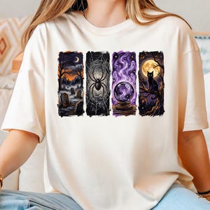 May include: A cream-coloured short-sleeve t-shirt featuring four rectangular graphic panels. The designs depict a graveyard at night, a spider on a web, a glowing purple crystal ball with swirling smoke, and a black cat perched on a tree branch.