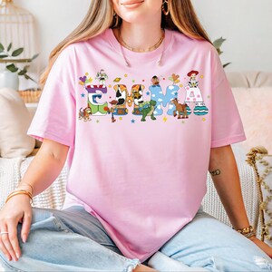 A woman wearing a pink t-shirt with a colorful graphic design of characters from Toy Story.