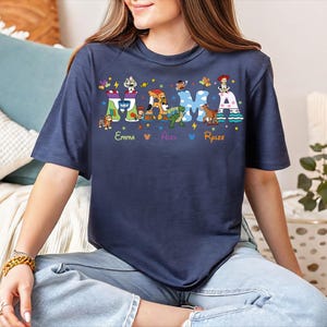 A woman wearing a blue t-shirt with a colorful graphic design of characters and text.