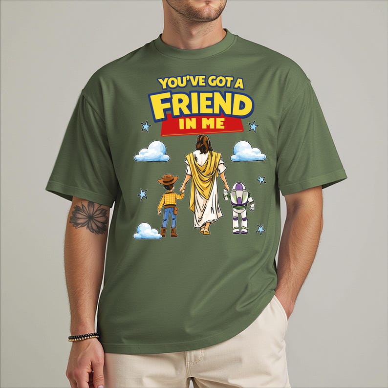 A green t-shirt with a graphic design depicting a person in a yellow robe and a child, along with a robot and clouds, along with the text "You've got a FRIEND in ME".