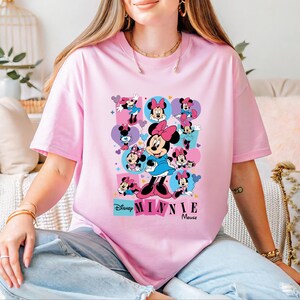 A woman wearing a pink t-shirt with Minnie Mouse printed on it, sitting on a couch.