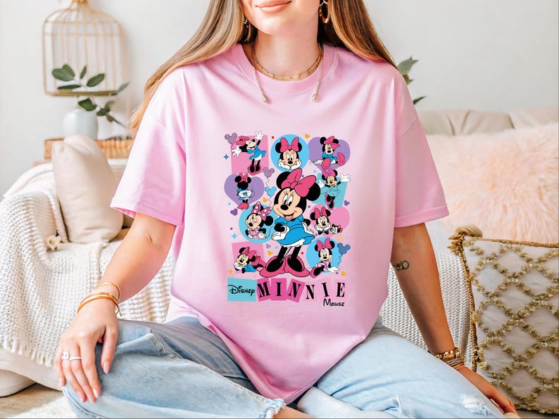 A woman wearing a pink t-shirt with Minnie Mouse printed on it, sitting on a couch.