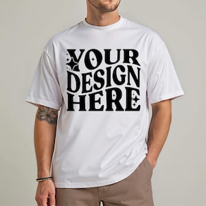 May include: White t-shirt with the text "YOUR DESIGN HERE" in a bold, black, retro-style font. The shirt has short sleeves and a relaxed fit. The design is centered on the front of the shirt.