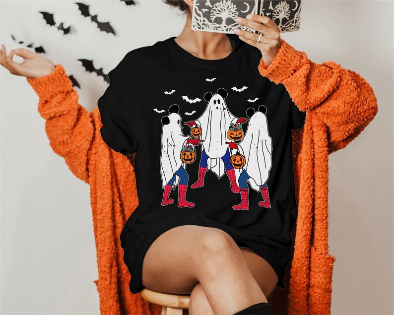 A person wearing a black t-shirt with a Halloween-themed graphic of ghostly figures and a spider-man character.