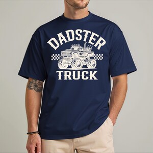 A man wearing a navy blue t-shirt with a graphic design of a monster truck and the text "DADSTER TRUCK" printed on it.