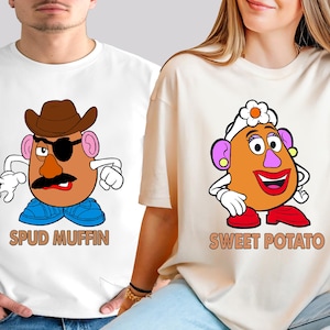 Könnte beinhalten: Zwei T-Shirts mit Cartoon-Kartoffelkopf-Charakteren. Ein Shirt zeigt einen Kartoffelkopf mit Cowboyhut, Augenklappe und dem Text "SPUD MUFFIN". Das andere Shirt hat einen Kartoffelkopf mit einer Blume und dem Text "SWEET POTATO".
