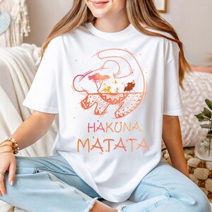 a woman sitting on a couch wearing a t - shirt that says hakona