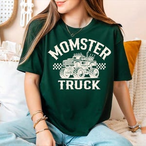 A woman wearing a green t-shirt with a graphic of a monster truck and the text "MOMSTER TRUCK" is sitting on a couch.