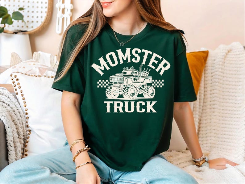 A woman wearing a green t-shirt with a graphic of a monster truck and the text "MOMSTER TRUCK" is sitting on a couch.