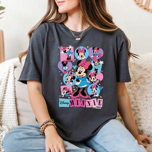 A woman wearing a t-shirt with a Minnie Mouse graphic is sitting on a couch.