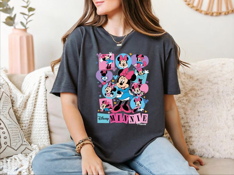A woman wearing a t-shirt with a Minnie Mouse graphic is sitting on a couch.