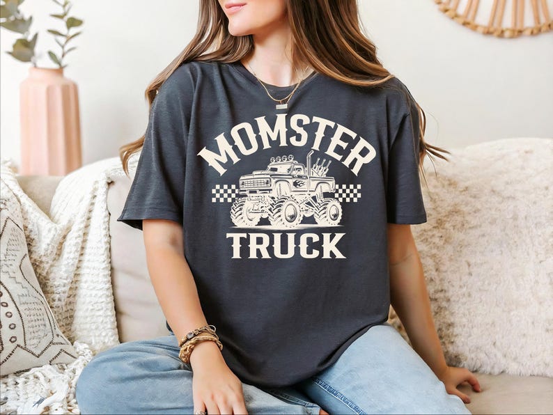 A woman wearing a black t-shirt with a graphic of a monster truck and the text "MOMSTER TRUCK" is sitting on a couch.