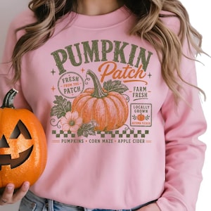 May include: A light pink crewneck sweatshirt featuring a graphic print with the text PUMPKIN Patch, FRESH FROM THE PATCH, FARM FRESH, LOCALLY GROWN, AUTUMN PICKED, PUMPKINS, CORN MAZE, APPLE CIDER, and an illustration of an orange pumpkin.