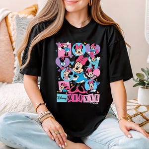A woman wearing a black t-shirt with a colorful graphic of Minnie Mouse and other Minnie Mouse characters.