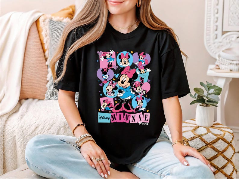 A woman wearing a black t-shirt with a colorful graphic of Minnie Mouse and other Minnie Mouse characters.