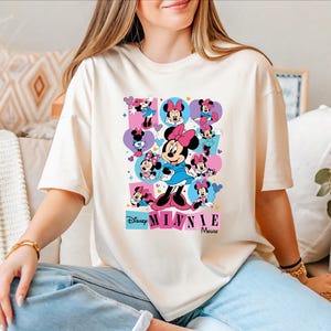 A woman wearing a white t-shirt with a Minnie Mouse graphic is sitting on a couch.