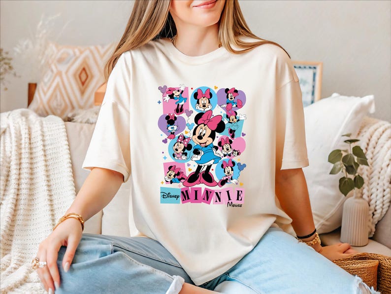 A woman wearing a white t-shirt with a Minnie Mouse graphic is sitting on a couch.