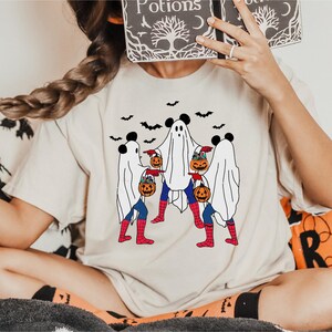 A person is sitting on a couch with a Halloween-themed t-shirt featuring a group of ghostly figures and jack-o-lanterns.
