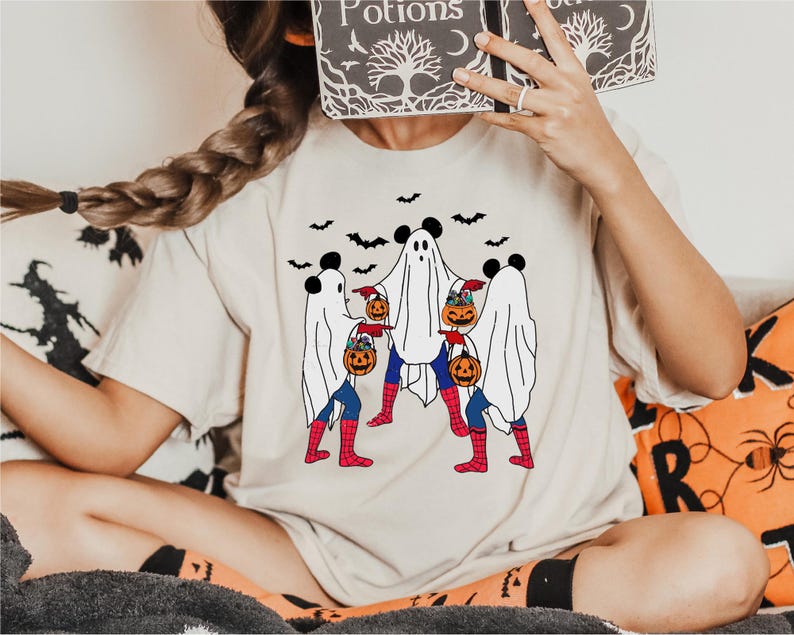A person is sitting on a couch with a Halloween-themed t-shirt featuring a group of ghostly figures and jack-o-lanterns.