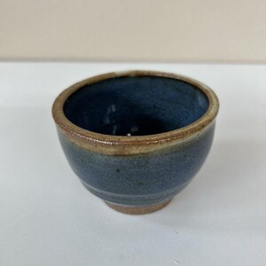 May include: A small, blue ceramic bowl with a brown rim. The bowl has a slightly textured surface and a rounded shape.