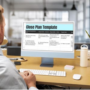 Op de afbeelding: Een persoon werkt op een computer met een "Close Plan Template". Het scherm toont een spreadsheet met kolommen voor actie-items, verantwoordelijken en streefdatums. Een toetsenbord, muis, waterfles en plant staan op het houten bureau.