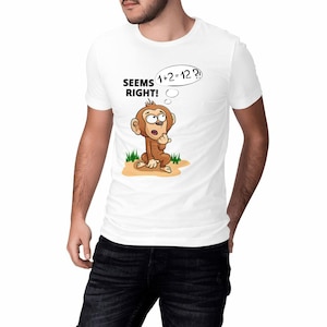 Könnte beinhalten: Weißes T-Shirt mit einem Cartoon-Affen, der über die Gleichung 1+2=12 nachdenkt. Der Text "SEEMS RIGHT!" steht über dem Affen, und die Gleichung befindet sich in einer Sprechblase. Der Affe ist braun und sitzt auf Sand.