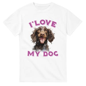 Peut inclure: Un t-shirt blanc à manches courtes avec un motif central représentant un chien brun de type épagneul, la gueule ouverte. Au-dessus du chien, le texte I LOVE est écrit en violet, et en dessous, le texte MY DOG en violet complète la phrase.