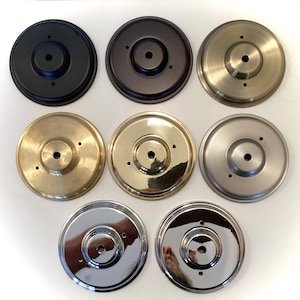 May include: A collection of eight circular metal ceiling canopy plates in various finishes. The finishes include black, bronze, brass, gold, brushed nickel, and chrome. Each plate has a central hole and three smaller holes.