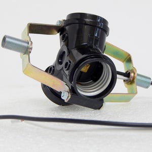 May include: A black light socket with a metal bracket and a threaded end. The socket has a white interior and is connected to a black wire. The bracket is gold-colored.