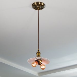 May include: A brass pendant light fixture with a white porcelain shade and two exposed light bulbs.