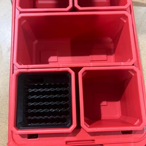 May include: A red plastic tool organizer with multiple compartments. The organizer has several open bins of varying sizes, including a black insert with a grid pattern. The overall design is functional and durable.
