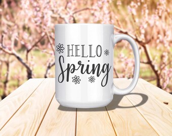 May include: White ceramic mug with a black design that says "Hello Spring" with small flower accents.