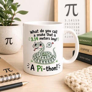 May include: A white ceramic mug featuring a cartoon snake illustration with a pattern of pi symbols. The text reads: What do you call a snake that is 3.14 metres long? A Pi-thon! The design includes a small speech bubble with a pi symbol and a heart.