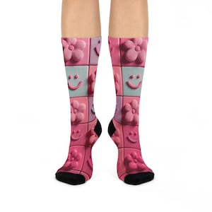 Puede incluir: Calcetines hasta la rodilla con un patrón repetido de flores rosas y caras sonrientes sobre un fondo de tablero de ajedrez. Los calcetines tienen talones y dedos negros, y los colores de fondo incluyen rosa, azul claro y lavanda.