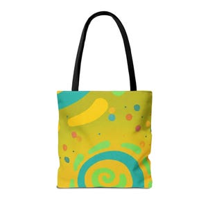 Puede incluir: Un bolso tote con fondo amarillo y un diseño abstracto colorido. El diseño incluye formas amarillas, turquesas y verdes, incluyendo una espiral, puntos y líneas curvas. El bolso tiene asas negras.